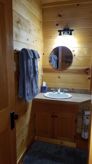 Un baño de cabaña de madera con lavamanos, espejo y toallas.