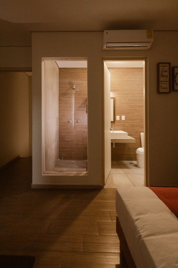 A bedroom with a wooden floor, a bed, a nightstand, and a bathroom visible through an open door. - Motel Puerta del Cielo (Oaxaca)