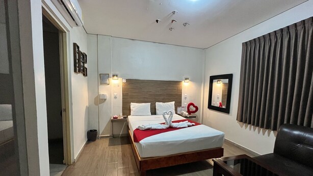 A hotel room with a wooden bed, a nightstand, a chair, a mirror, and a red heart-shaped decoration on the nightstand. - Motel Puerta del Cielo (Oaxaca)