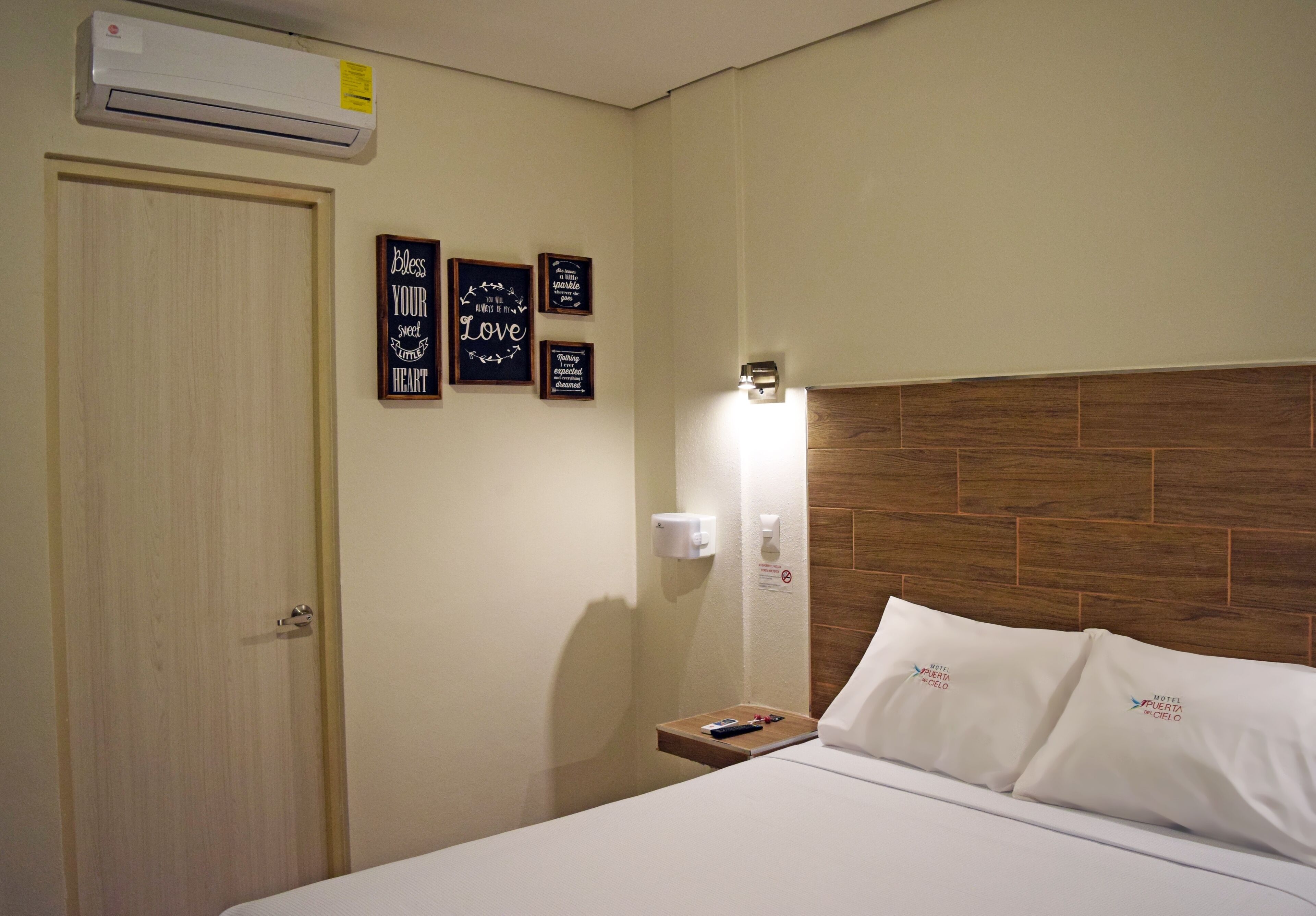 Ein Hotelzimmer mit hölzernem Kopfteil, einem Nachttisch mit Fernbedienung und einer Wandklimaanlage.