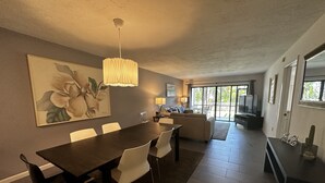 A modern living room with a dining area, a large painting, and a view to the outside. - Contemporary Garden View, Ground Floor Unit, Short Walk to Pool/Beach (Siesta Key)