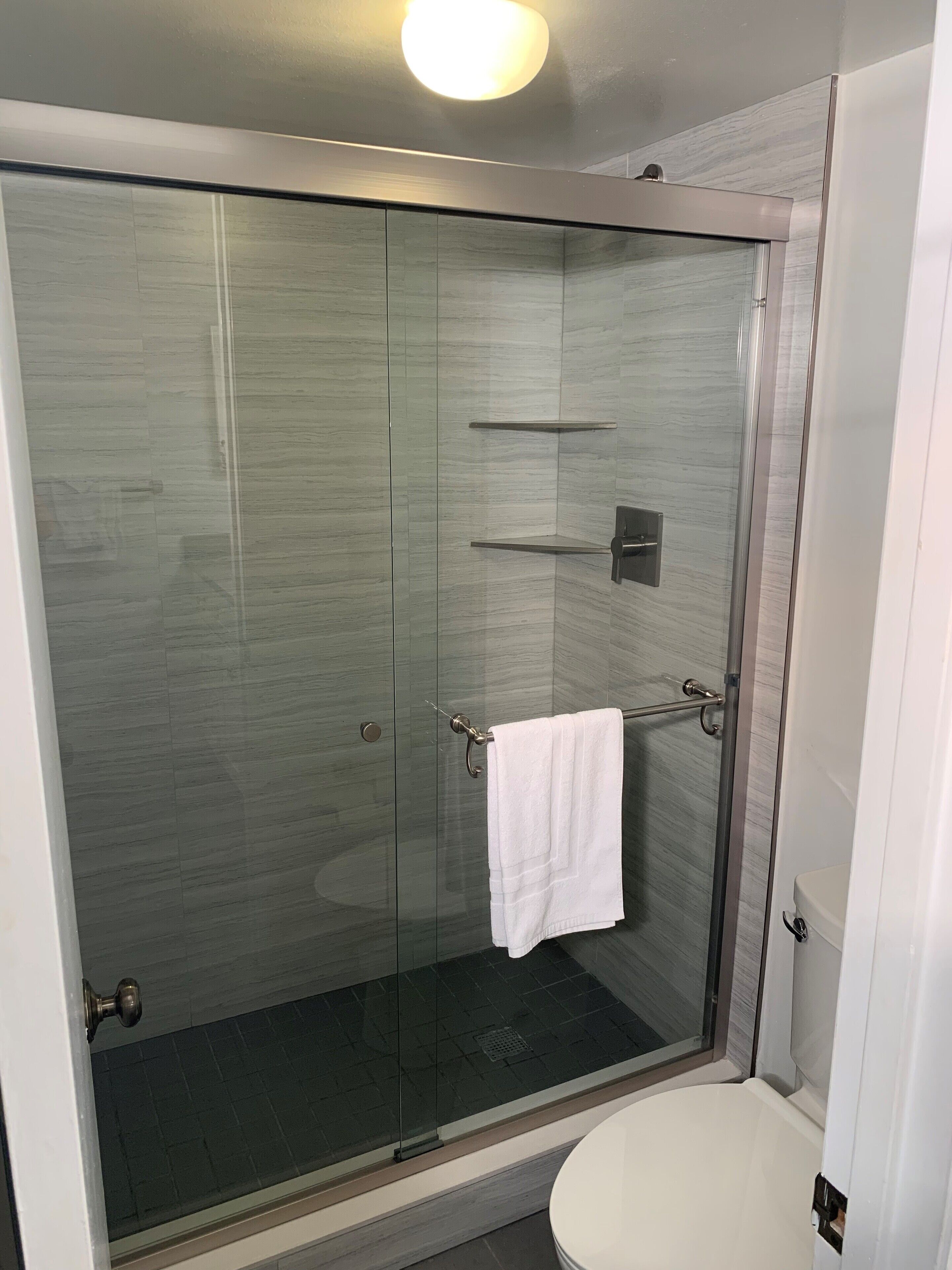 Ein modernes Badezimmer mit einer einteiligen Glasdusche, einer weißen Toilette und einem Handtuchhalter.
