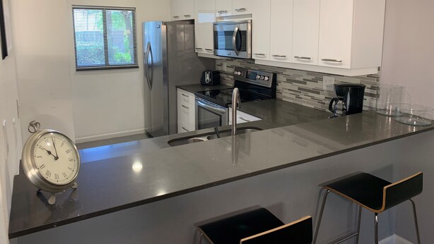 A modern kitchen with white cabinets, stainless steel appliances, a black countertop, and a built-in oven. - Contemporary Garden View, Ground Floor Unit, Short Walk to Pool/Beach (Siesta Key)