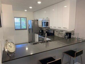 A modern kitchen with white cabinets, stainless steel appliances, a black countertop, and a built-in oven. - Contemporary Garden View, Ground Floor Unit, Short Walk to Pool/Beach (Siesta Key)