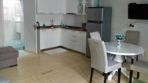 Una cocina moderna con armarios blancos, un refrigerador de acero inoxidable y un comedor con una mesa blanca y cuatro sillas.