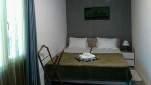 Habitación de hotel con cama, mesita de noche, lámpara, silla y un cuadro en la pared.