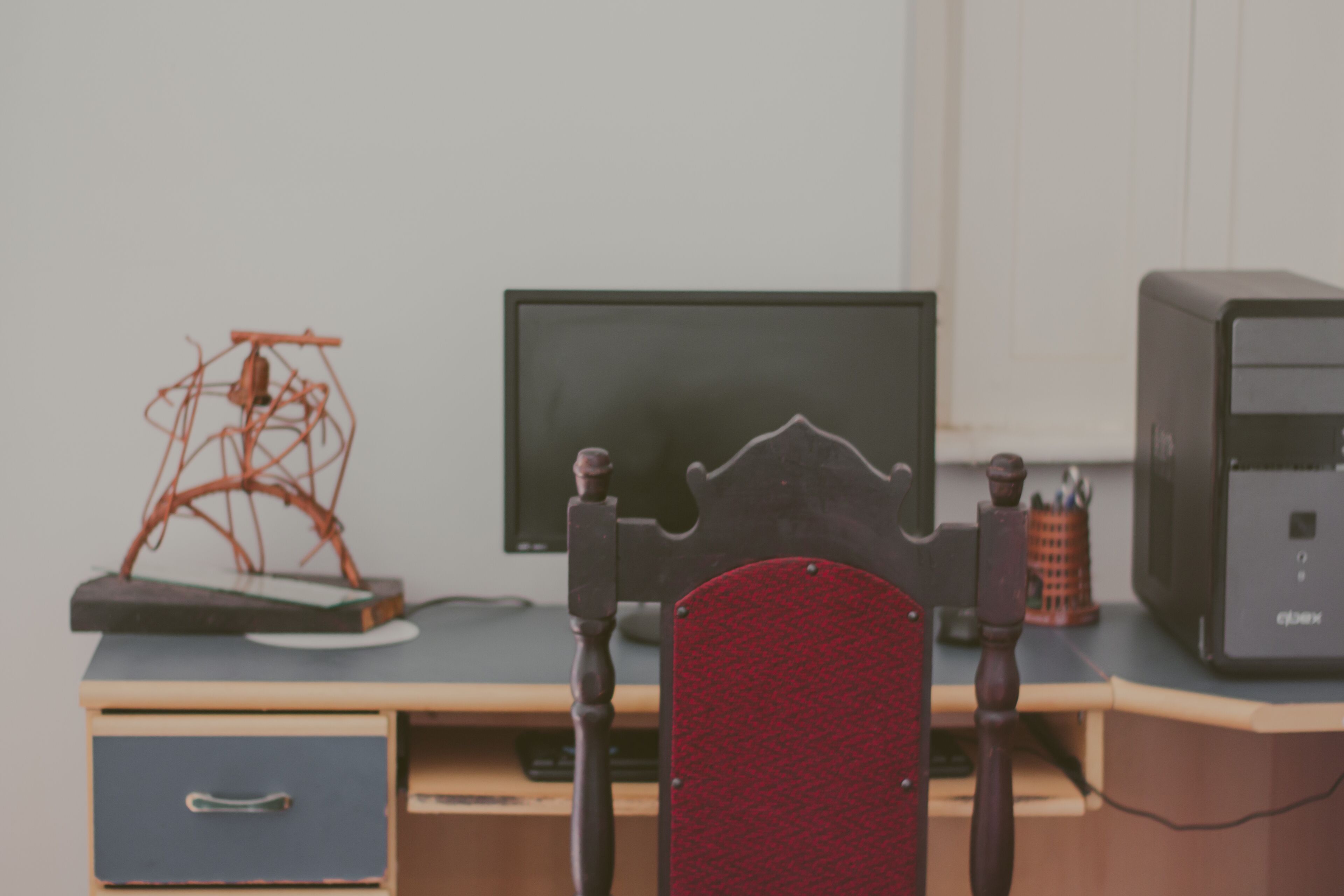 Un bureau en bois avec un écran d’ordinateur, un ordinateur de bureau et une chaise rouge.