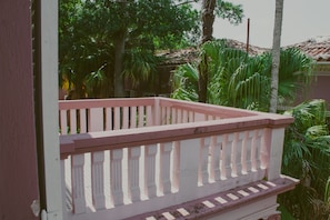 Un balcon doté d’une balustrade blanche, entouré d’une végétation luxuriante et de palmiers.