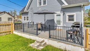 A residential house with a patio area featuring a grill, outdoor furniture, and a black umbrella. - The Junction: Victorian Home in Quaint Fortville! (Fortville)