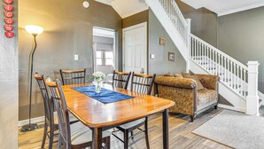 A dining area with a wooden table, chairs, and a blue placemat. There is a staircase with a white railing leading to another room. - The Junction: Victorian Home in Quaint Fortville! (Fortville)