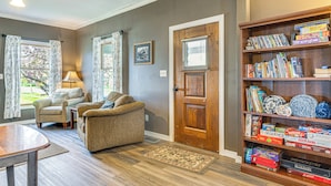 A living room with a sofa, armchairs, a wooden bookshelf, and a dining table. - The Junction: Victorian Home in Quaint Fortville! (Fortville)