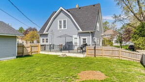 A two-story house with a grey roof, a front porch, and a fenced backyard. - The Junction: Victorian Home in Quaint Fortville! (Fortville)