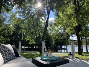 Un patio con un sofá, una mesa con una botella y vasos, y vista a un lago.