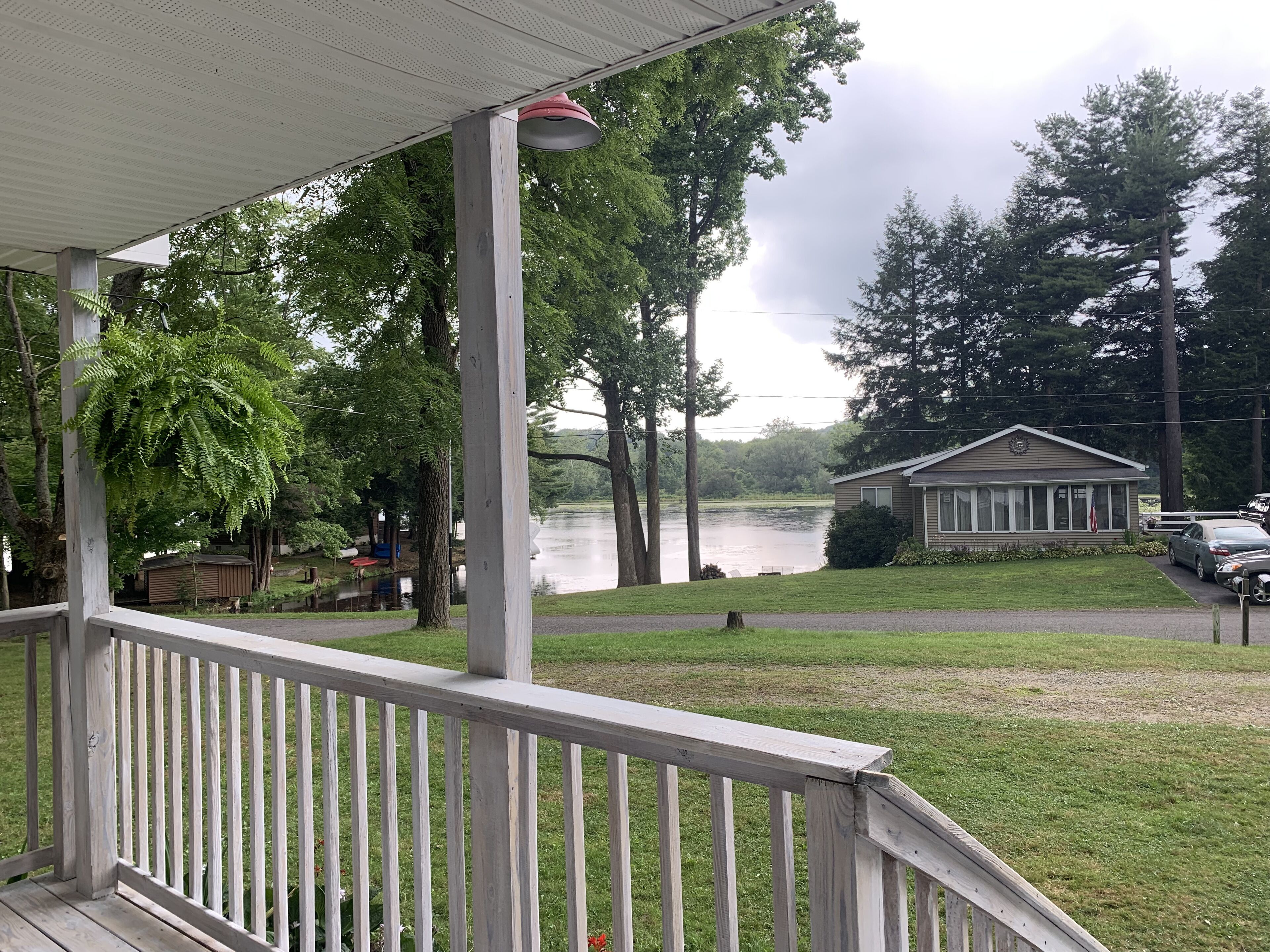 A wooden deck with a railing, a gazebo, a lake, and a small building with a flag.