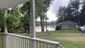 A wooden deck with a railing, a gazebo, a lake, and a small building with a flag.