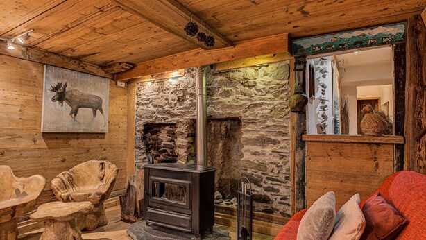 A rustic interior with a stone fireplace, wooden furniture, and a painting of a moose. - Chalet Pele - Alpes Agency - Central Chamonix - Sleeps 11 (Chamonix)
