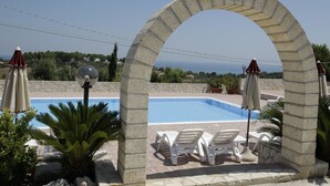 A swimming pool with white lounge chairs and umbrellas, framed by a stone archway. - Villa Hibiscus - Panoramic studio for 2 people in a villa with pool (Vieste)