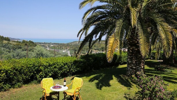 A patio with two yellow chairs and a table, overlooking a lush garden and a coastal view. - Villa Hibiscus - Panoramic studio for 2 people in a villa with pool (Vieste)