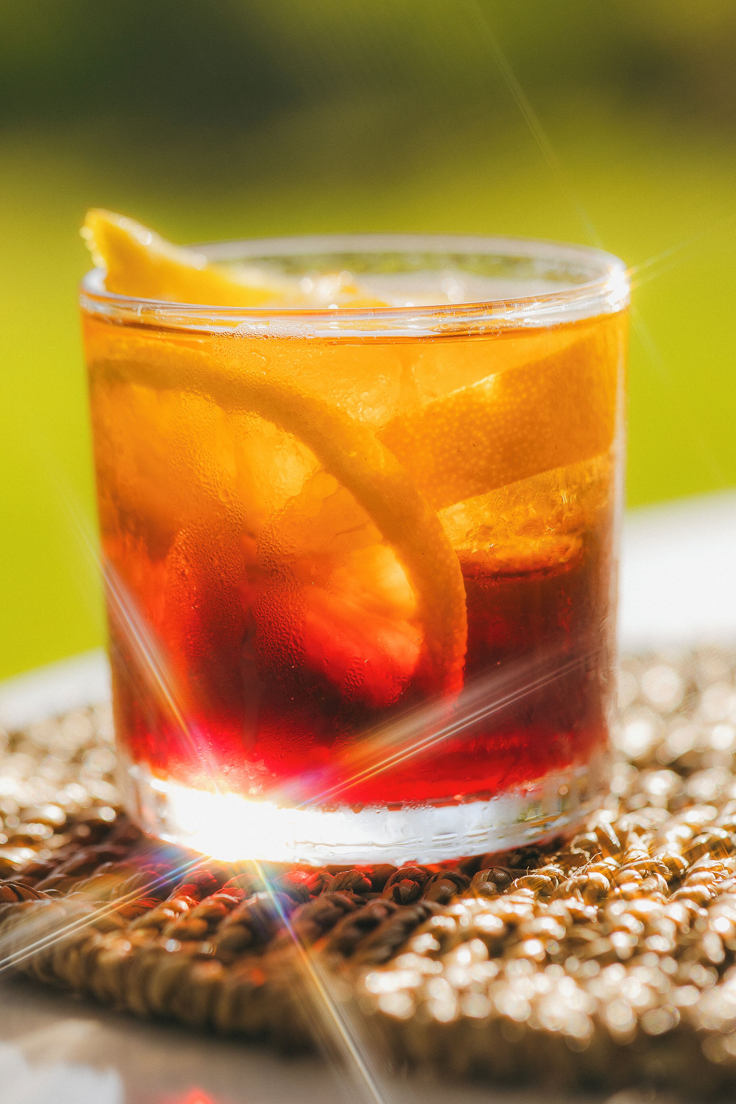 A glass with a beverage and a slice of fruit on a woven surface.