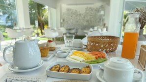 A breakfast table with a teapot, cups, a basket of fruit, and a bottle of orange juice.