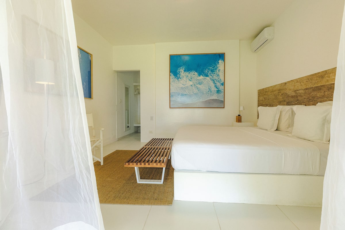 Un dormitorio con cama, un banco, un cuadro y una puerta que da a otra habitación.