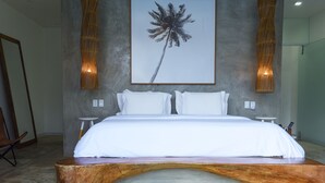 A modern bedroom with a large bed, a wooden bench, and a framed palm tree artwork on the wall.