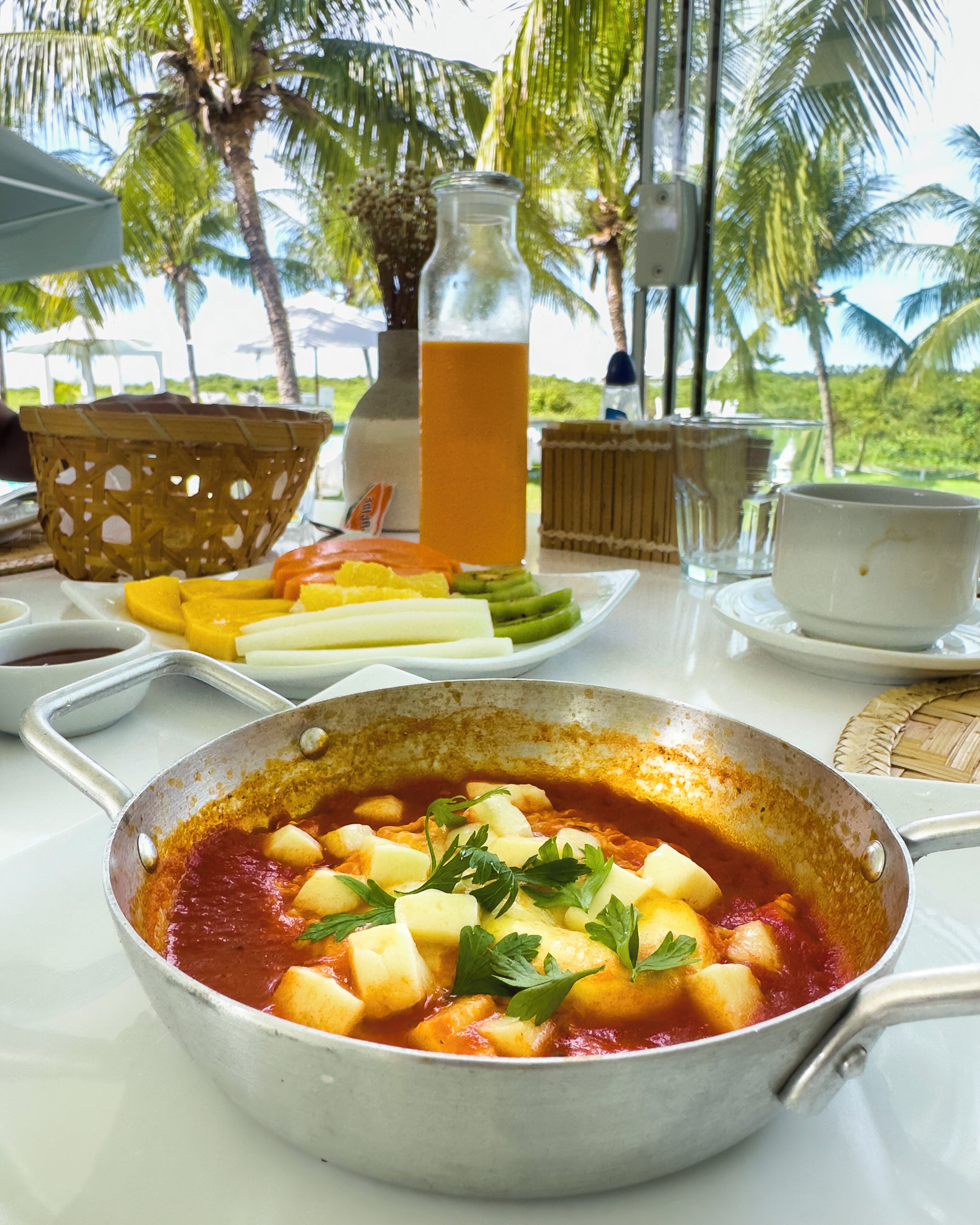 A table with a meal, a glass of juice, and a view of palm trees.