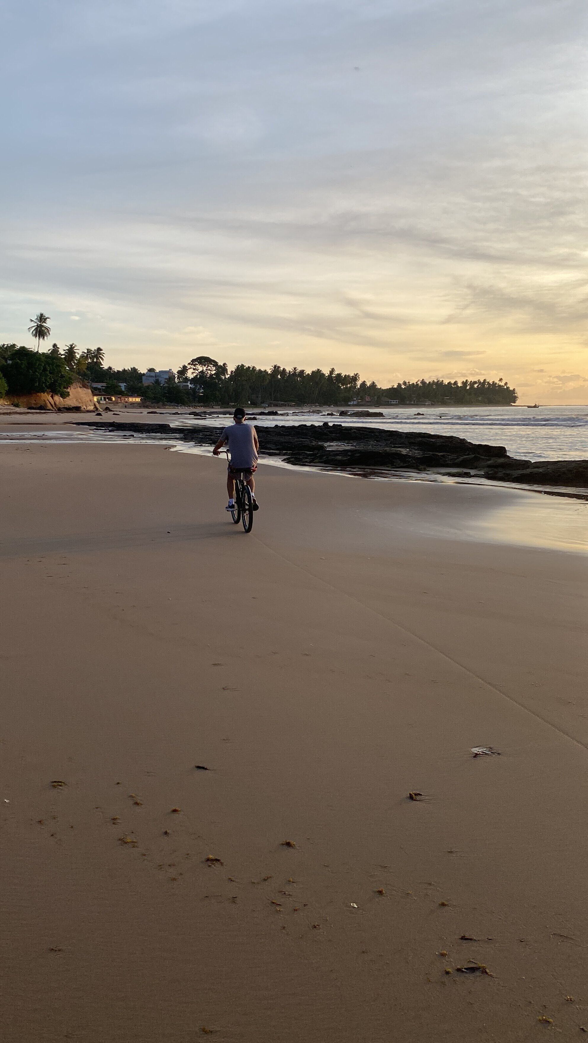 A wide sandy beach with a person riding a bicycle.