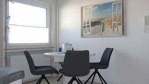 Una habitación con ventana, un cuadro, una mesa con sillas y una mesita blanca.