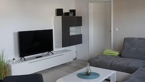 Una sala de estar moderna con un televisor de pantalla plana montado en una pared blanca, un sofá gris y una mesa de centro blanca con un objeto decorativo encima.