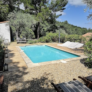 Ein rechteckiger Pool, umgeben von einer Holzterrasse, mit einer überdachten Sitzgelegenheit und einer Pergola darüber.
