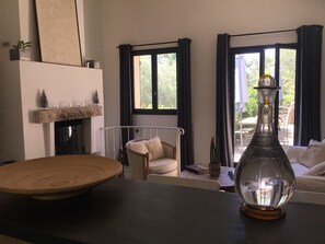 Un salon doté d’une cheminée, d’une table à manger, d’un canapé et offrant une vue sur l’extérieur grâce à de grandes fenêtres.
