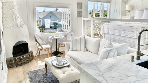 Un salón moderno con una decoración en tonos blancos, una chimenea, un sofá, un comedor y vistas al exterior.