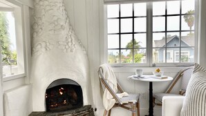Rincón acogedor con chimenea de piedra, sillones de mimbre, una mesita redonda y una ventana con vistas a casas.