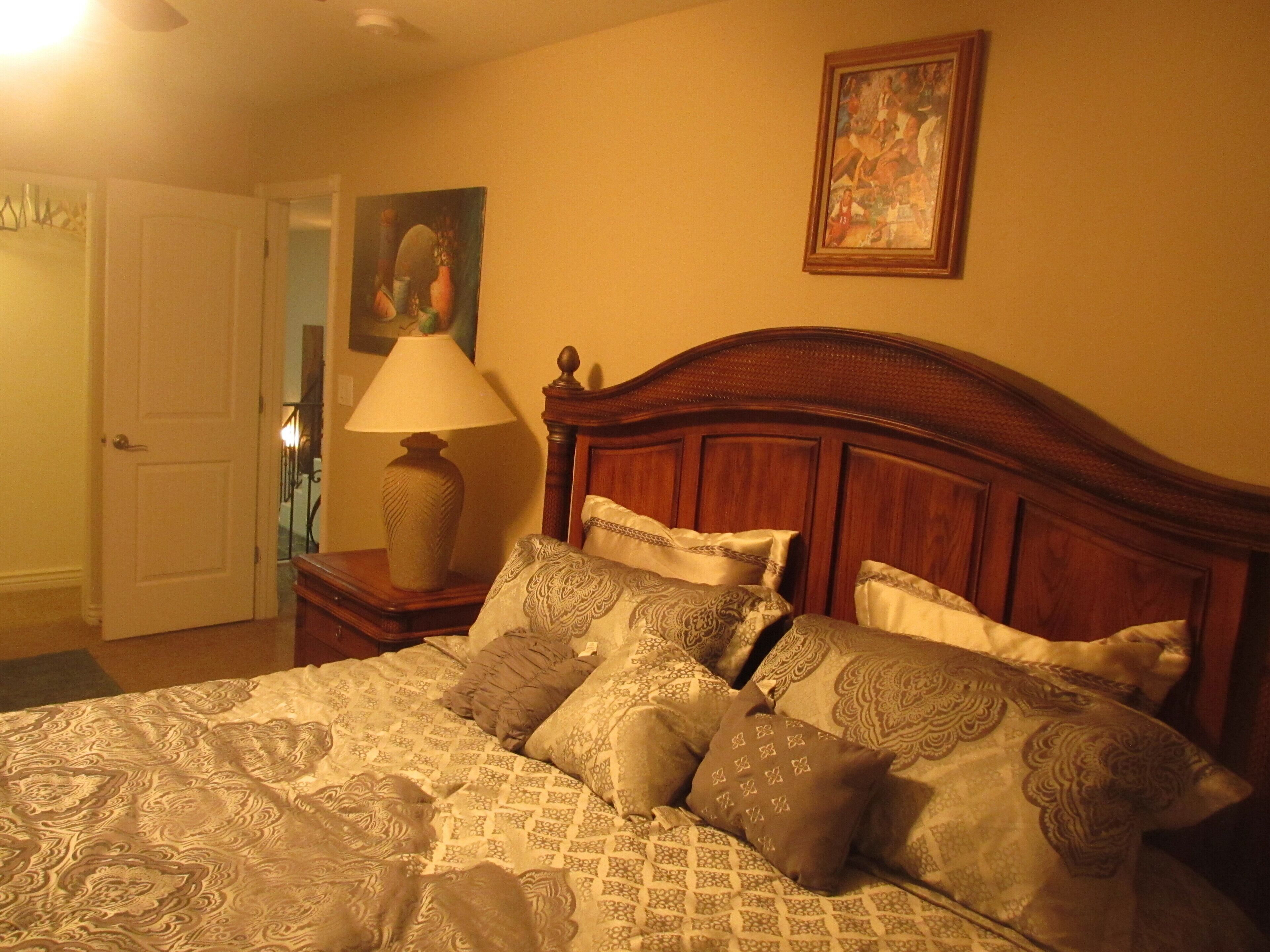 A bedroom with a wooden headboard, patterned bedding, a bedside lamp, and a painting on the wall.