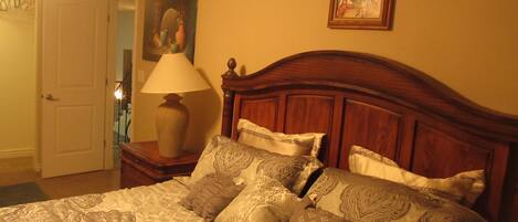 A bedroom with a wooden headboard, patterned bedding, a bedside lamp, and a painting on the wall.