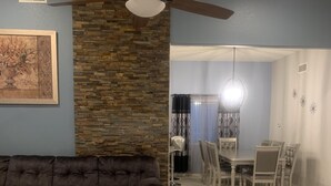 A living room with a dark brown sofa, a glass coffee table, and a dining area with a table and chairs.