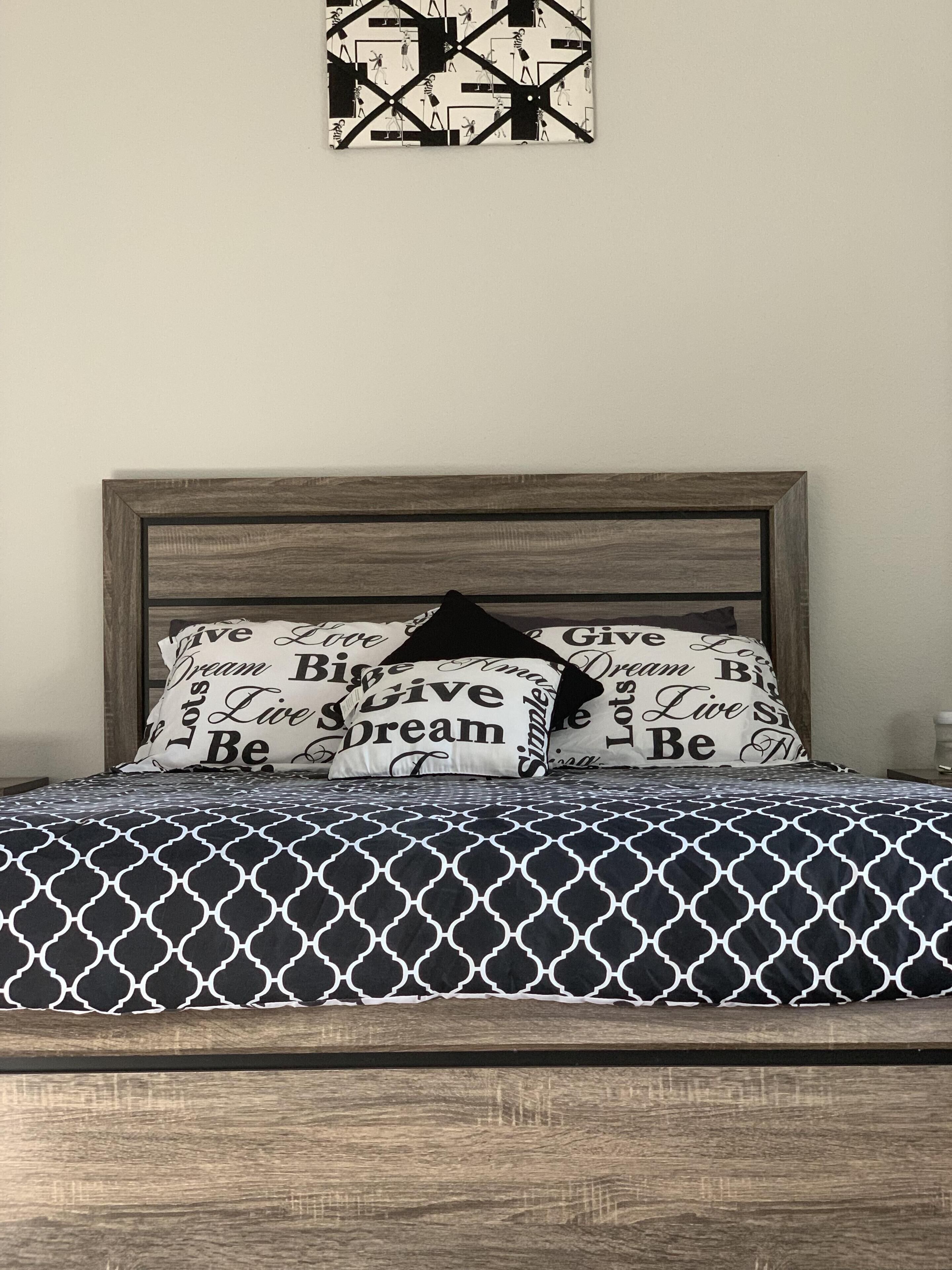 A bed with a patterned bedspread, two pillows with motivational text, and a geometric wall decoration.