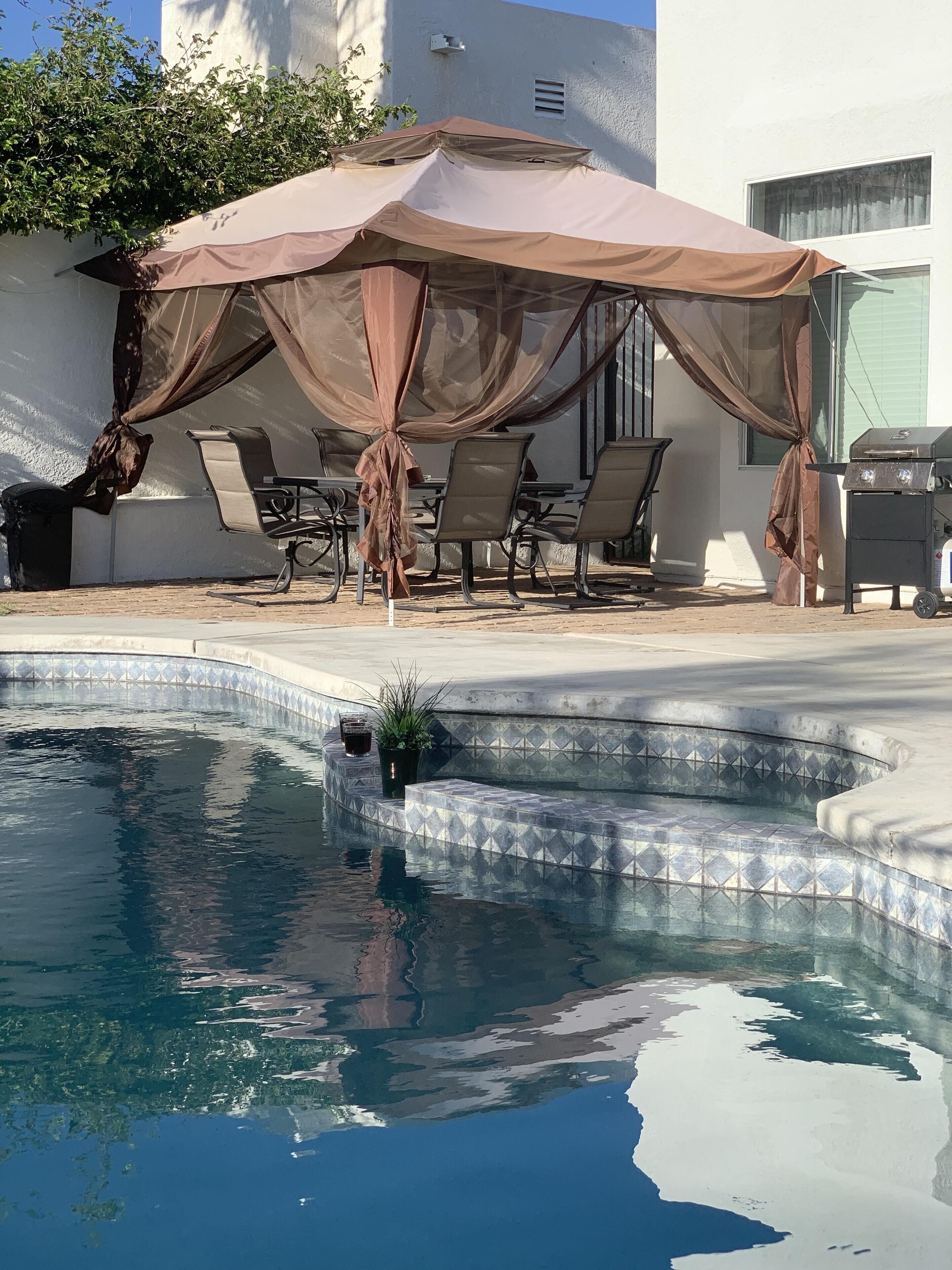 A swimming pool with a sunshade and lounge chairs.