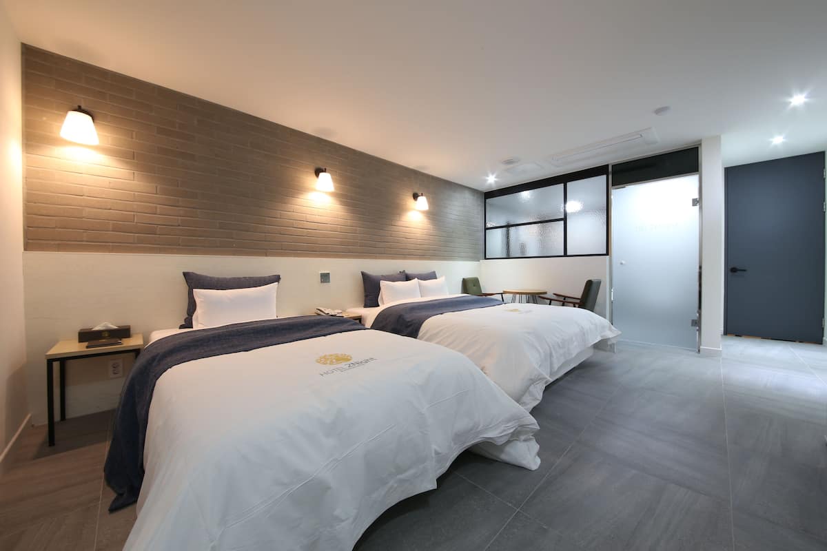 Una habitación de hotel moderna con dos camas, una pared de acento de madera y un ventanal grande.