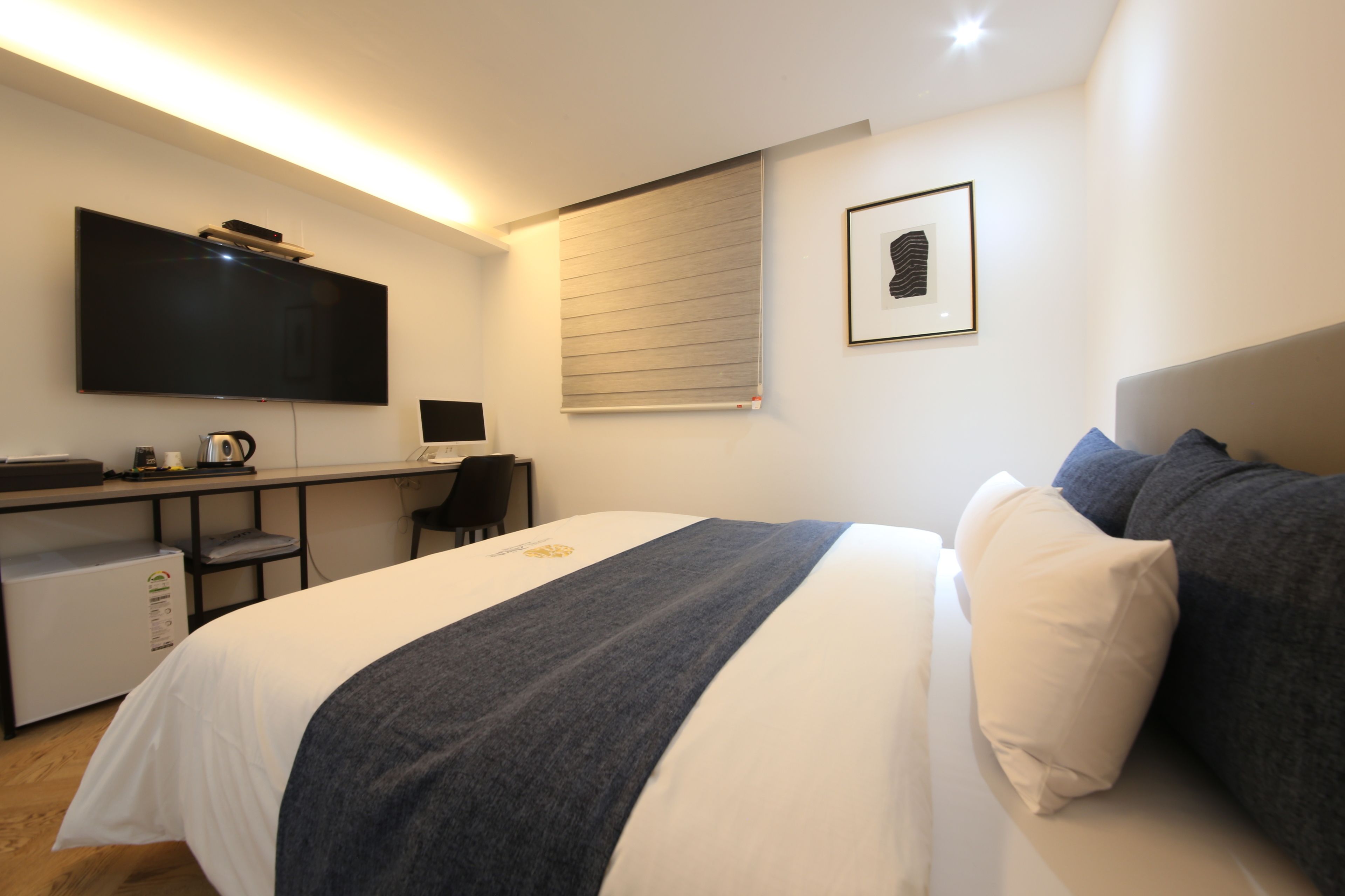 A hotel room with a bed, a desk with a computer, a television, and a window with blinds.