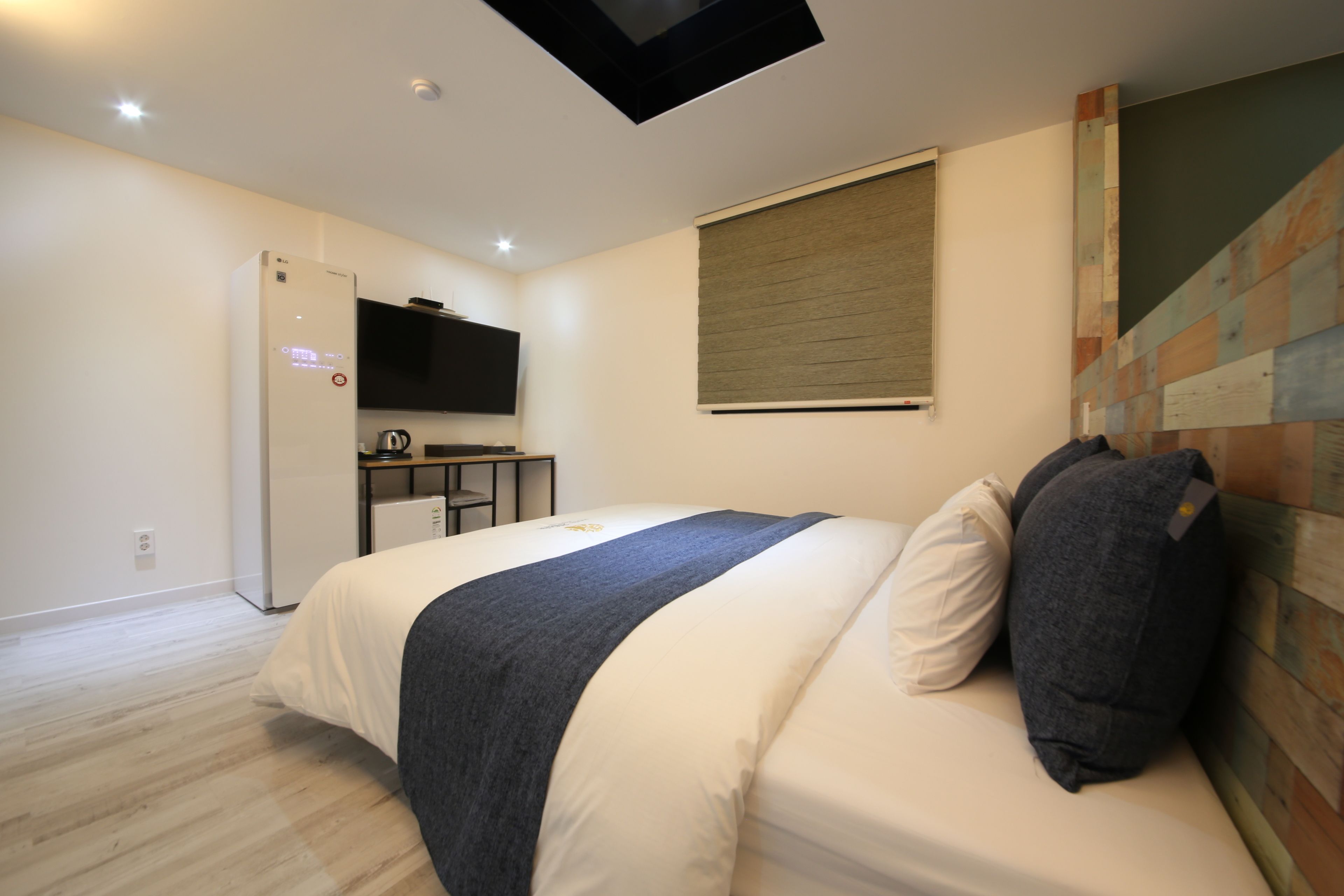 A modern bedroom with a bed, a flat-screen TV, a desk, and a window with blinds.