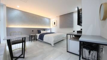 A modern hotel room with a bed, bedside table, desk, and chair.