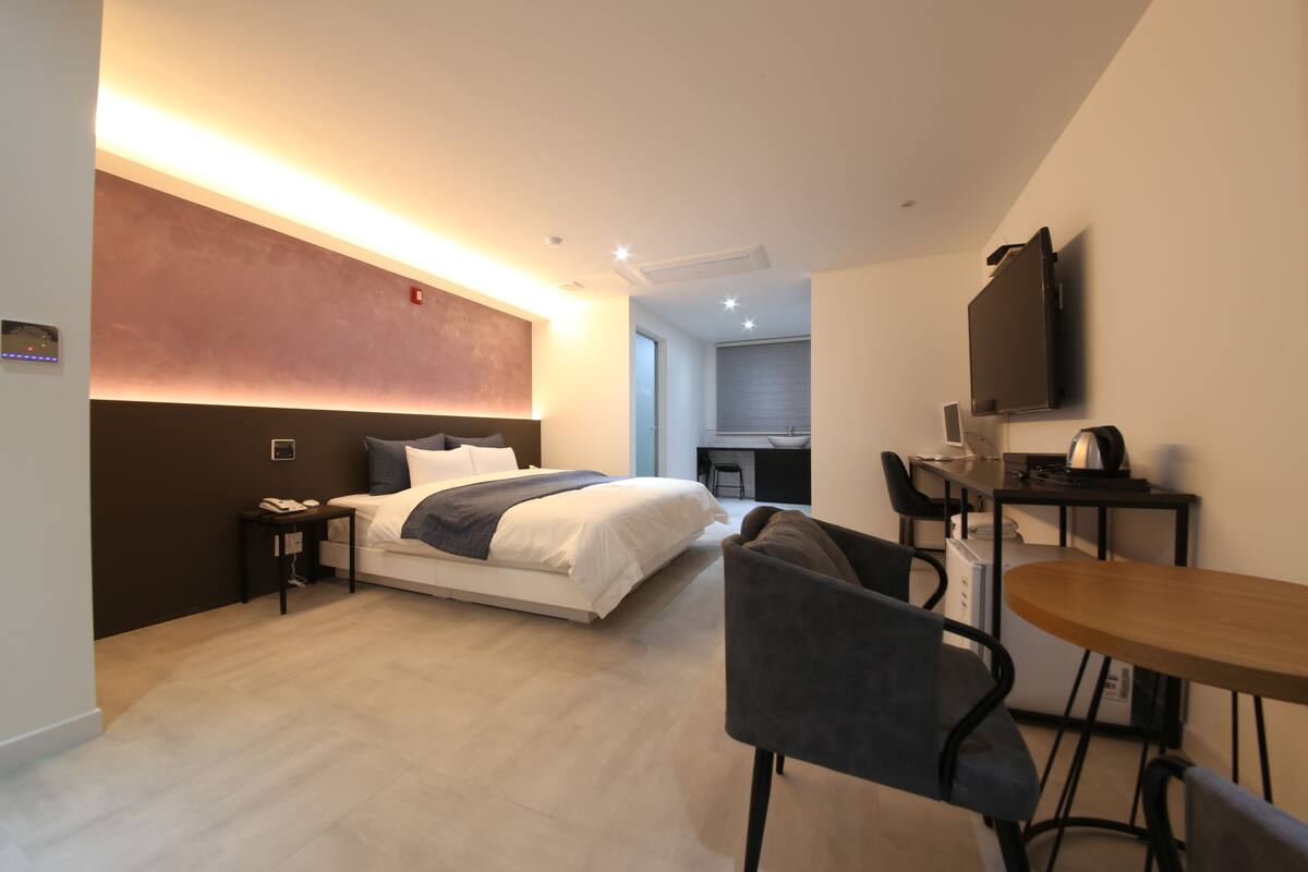 Una habitación de hotel moderna con cama, mesita de noche, silla, escritorio y televisor de pantalla plana.
