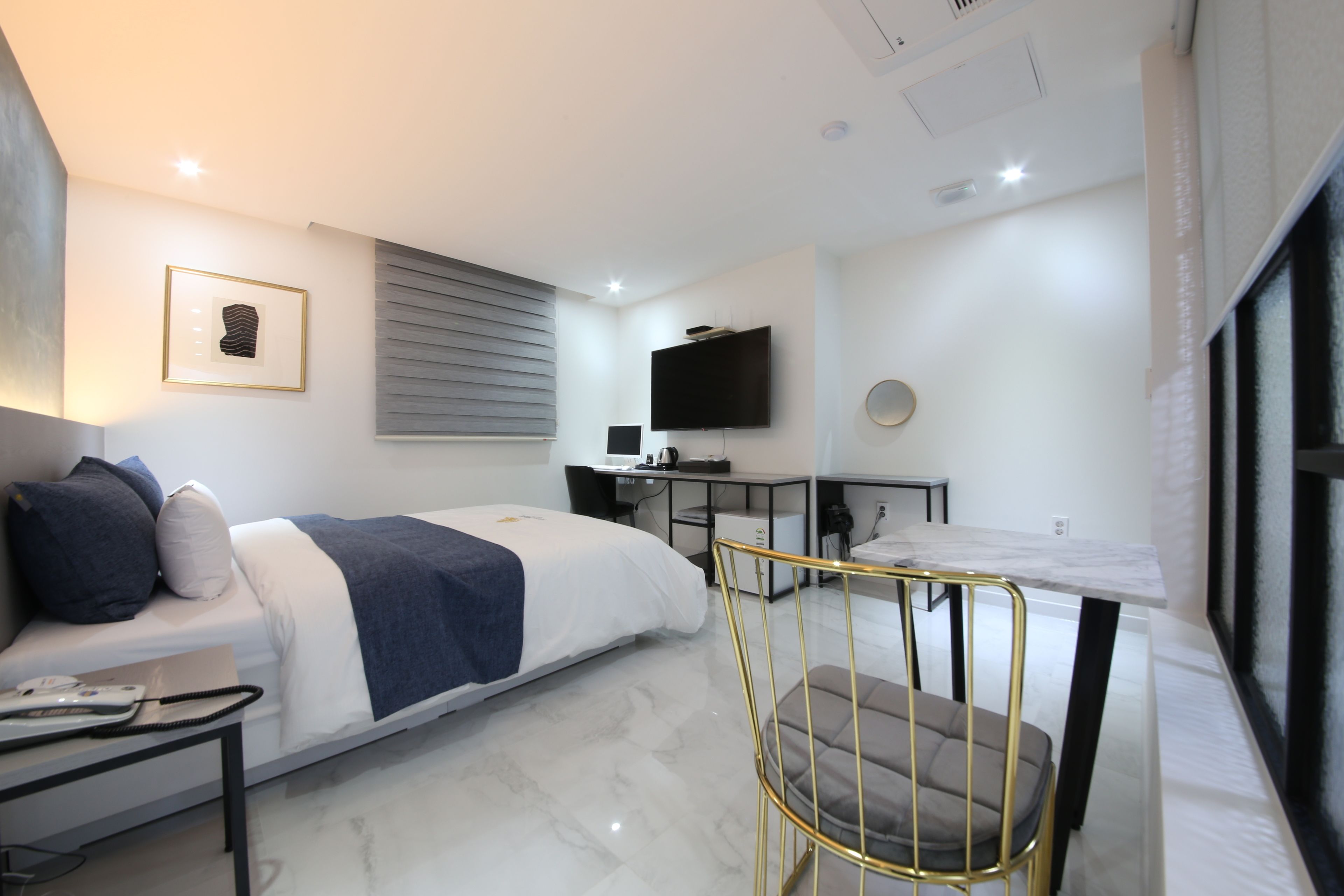 Une chambre d’hôtel moderne équipée d’un lit, d’un bureau, d’une chaise, d’une télévision et d’une fenêtre avec des stores.