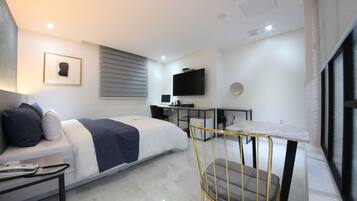 Une chambre d’hôtel moderne équipée d’un lit, d’un bureau, d’une chaise, d’une télévision et d’une fenêtre avec des stores.