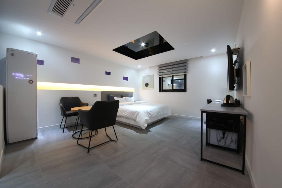 Una habitación de hotel moderna con cama, escritorio con silla, kitchenette pequeña y lámpara en el techo.