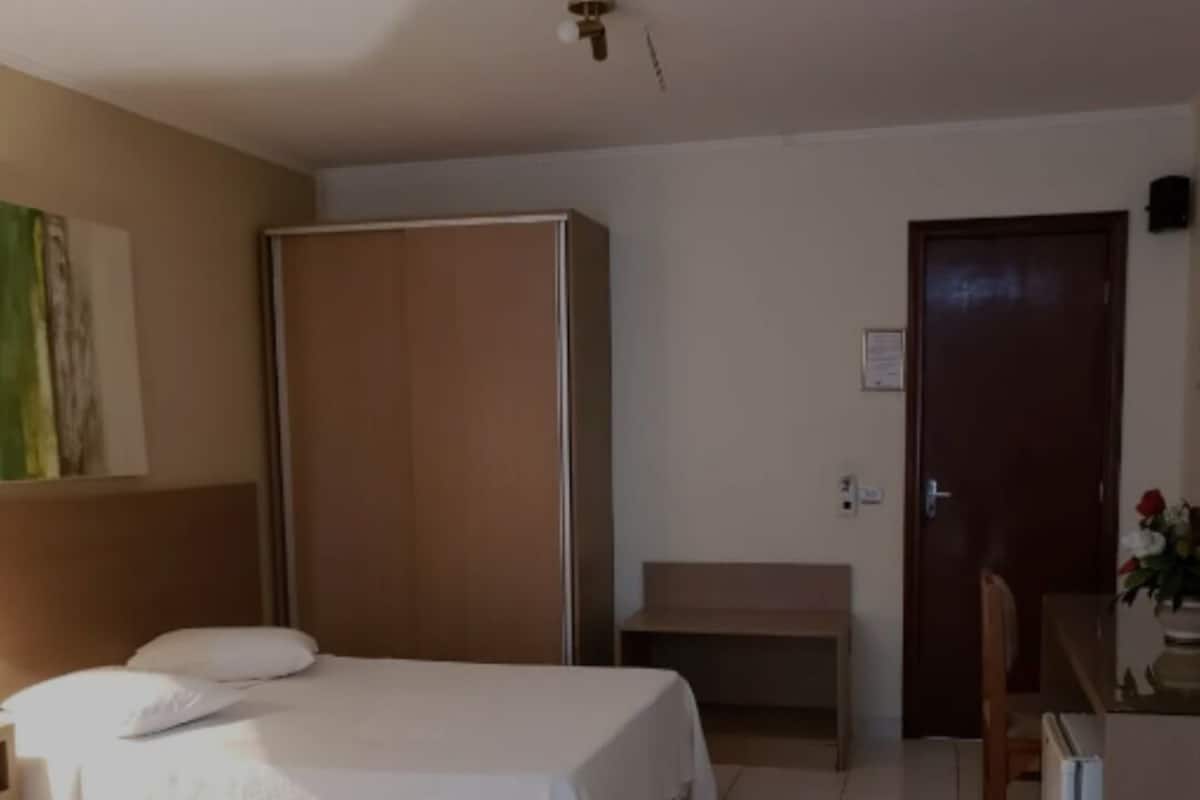 A bedroom with a bed, a wardrobe, a desk, and a chair.