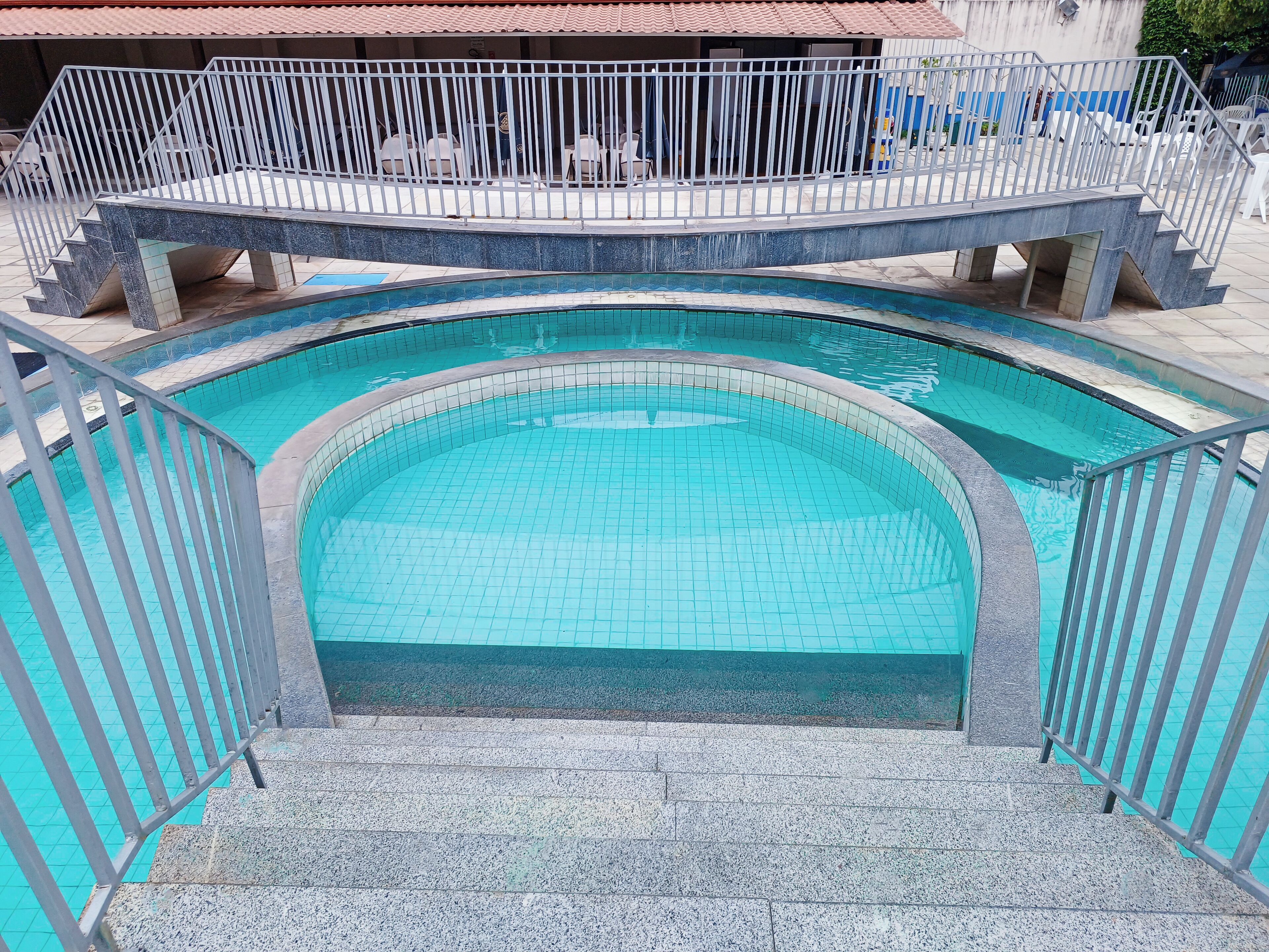Piscina com deck revestido e grades de metal.