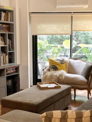 Un salon moderne avec un canapé, un pouf et une bibliothèque.